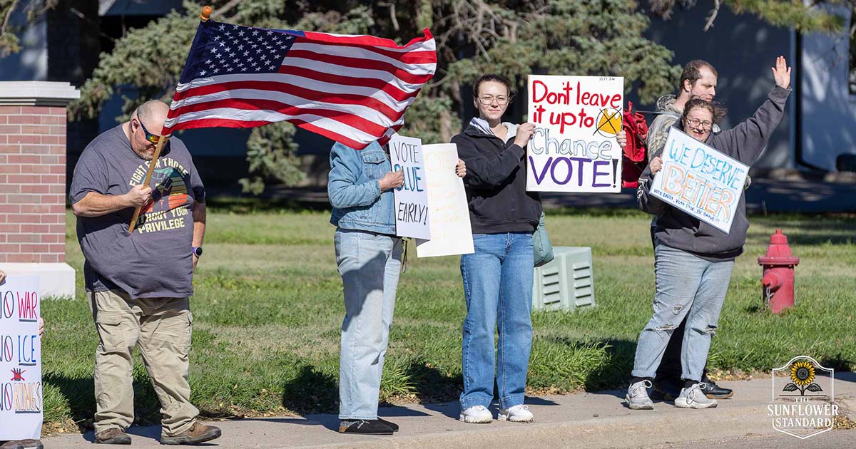 Participants hold signs and an American flag during the No Kings protest along Range Avenue in Colby